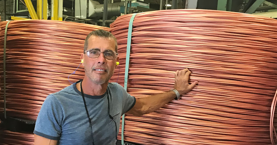 Gene Brown beside reels of copper wire in a cable plant